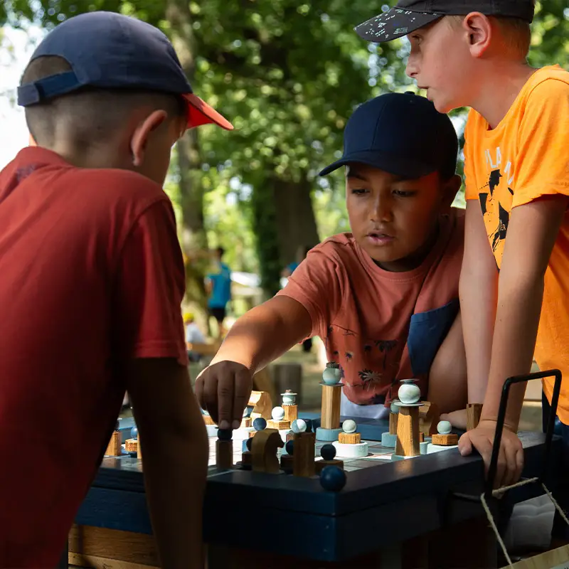 trois ados réunis autour d'une partie d'échecs XXL dans un parc de jeux en plein air - Au Grand Air (Ain)
