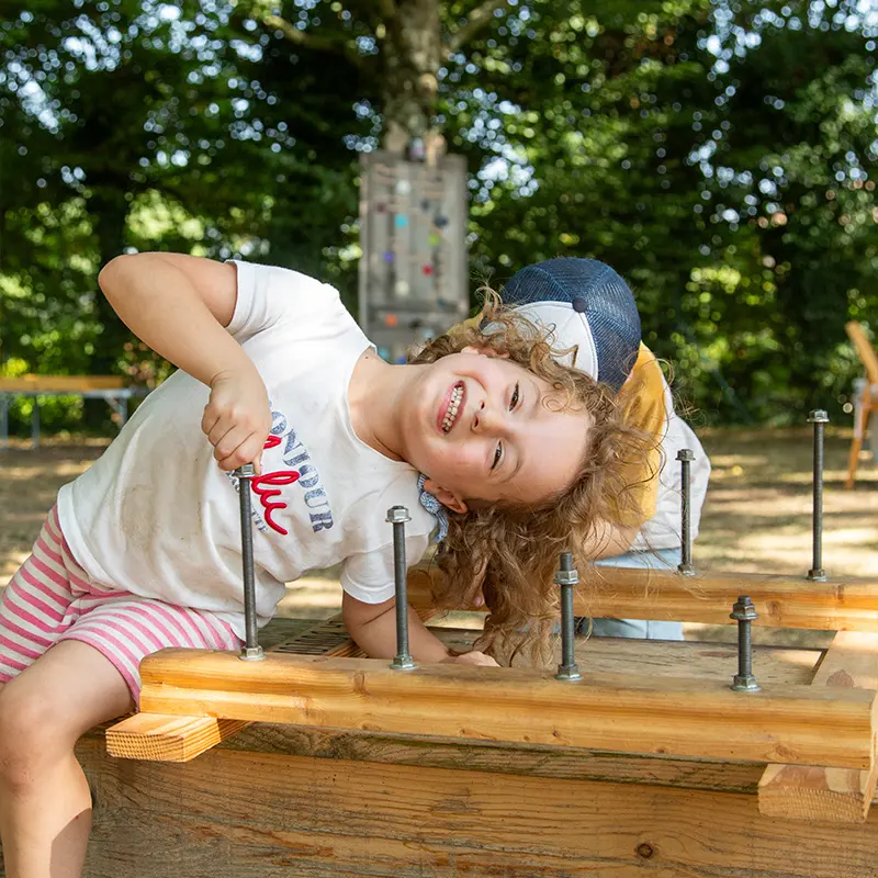 une petite fille sourit en jouant au jeu en bois Boulonn'rit - Au Grand Air, Vonnas